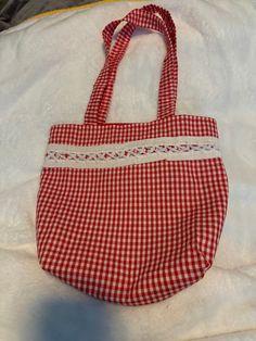 a red and white gingham bag sitting on top of a bed next to a pillow