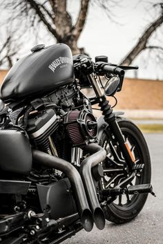 a black motorcycle parked on the street next to a tree and building in the background