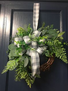 a wreath hanging on the front door with greenery and ribbon tied around it's edges