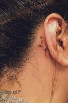 a woman's ear has a small flower tattoo on it