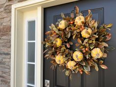 a wreath on the front door of a house with leaves and pumpkins hanging from it