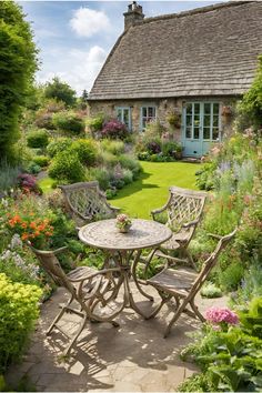 a table and chairs in the middle of a garden with lots of flowers around it