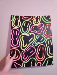 a hand is holding up a piece of art with neon colors on black and white paper