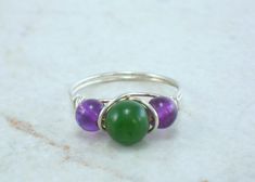 Nephrite Jade and Amethyst Sterling Silver Bead Ring This ring is handcrafted with a 6 mm Nephrite Jade and two Amethyst beads on sterling silver wire. This is a representation of the ring you will receive. With being real gemstones, there are variations in all gems, so please keep that in mind. This ring can be made for any size from 2 to 15 including half sizes. The picture is enlarged to show detail. Once made, these rings can not be re-sized. Metaphysical Properties of Jade - The ancient Chi Adjustable Green Amethyst Jewelry, Handmade Green Amethyst Gemstones, Green Amethyst Round Bead Jewelry, Green Amethyst Beaded Jewelry, All Gems, Nephrite Jade, Amethyst Beads, Silver Bead, Beaded Rings