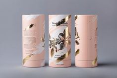 three pink and gold tube packagings on a grey background, each with an image of flowers