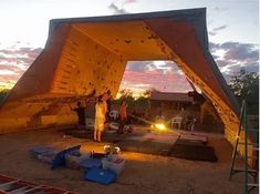 a group of people standing in front of a tent at night with the sun setting