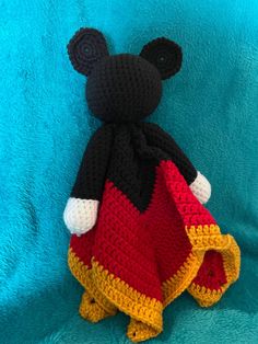 a crocheted mickey mouse sitting on top of a blue blanket in the shape of a red and yellow dress