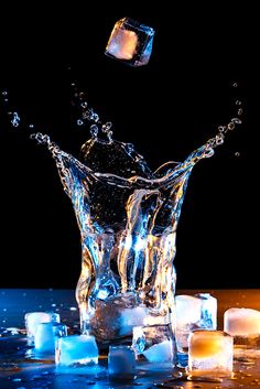 ice cubes and water splashing into a glass on a table with lit candles