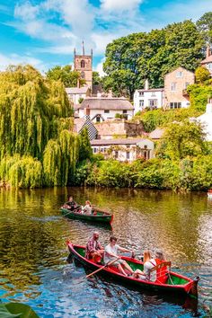 two boats with people on them floating down a river in front of houses and trees