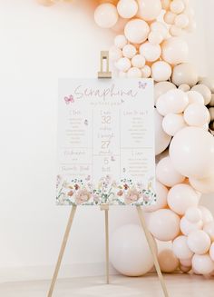 a sign that is next to balloons and a wall with flowers on it, sitting in front of a white backdrop