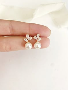 a person is holding two pearl and diamond earrings in their hand, both with white pearls on them