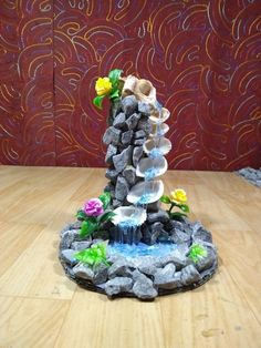 a fountain made out of rocks and flowers on a wooden table with a red wall in the background