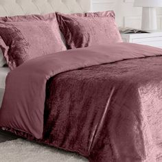 a bed with pink comforter and pillows in a white room next to a night stand