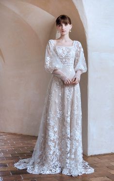 a woman standing in front of a wall wearing a dress with long sleeves and flowers on it