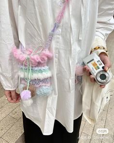 a person holding a camera in their hand while wearing a white shirt and black pants