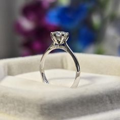 a close up of a diamond ring on a white box with flowers in the background