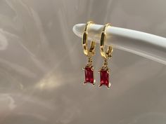 Ruby red dangly hoop earrings Gold plated brass hoop earrings Hoop size approximately 13mm Ruby red cubic zirconia charm size approximately 8mm x 4mm Every item comes in our frosted travel pouch  Gift wrap pouch & box set available, also sold separately Fancy Earrings Gold Small, Gold And Red Earrings Dangle, Ruby Earrings Aesthetic, Red Gem Earrings, Jewelry For Red Dress Formal, Red Dangly Earrings, Gold And Ruby Earrings, Red Prom Dress Gold Jewelry, Red Dress Accessories Jewelry Formal