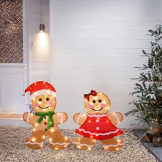 two lighted gingerbread men standing next to a christmas tree