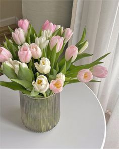 a vase filled with pink and white tulips on top of a round table