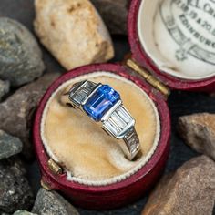 This gorgeous ring is centered with one (1) emerald cut tanzanite set into a channel. The ring is also accented with sixteen (16) baguette cut diamonds set into channels. The ring measures 6.8mm at the top, rises 5.5mm above the finger, tapering to 2.4mm wide and 1.0mm thick at the base of the shank. This ring is currently a size 5. Rectangular Brilliant Cut Sapphire Ring For Formal Occasions, Luxury Tanzanite Diamond Ring With Emerald Cut, Luxury Tanzanite Emerald Cut Ring, Art Deco Sapphire Ring With Baguette And Brilliant Cut, Timeless Sapphire Ring With Diamond Baguette Cut, Timeless Sapphire Baguette Cut Ring, Timeless Sapphire Baguette Cut Ring With Diamond Details, Classic Gia Certified Rectangular Sapphire Ring, Art Deco Sapphire Ring With Baguette Cut Center Stone