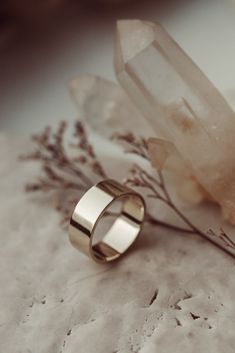 two gold wedding rings sitting on top of a table next to a crystal rock and flower