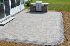 an outdoor kitchen and grill area with brick pavers in the foreground, surrounded by grass