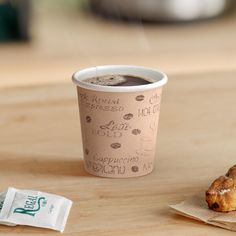 a cup of coffee sitting on top of a wooden table next to a donut