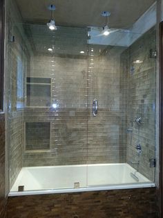 a glass shower door in a bathroom with wood flooring and tile on the walls