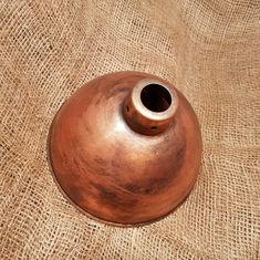 a brown vase sitting on top of a burlock covered tablecloth next to a cup