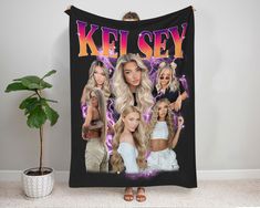 a woman with blonde hair is standing in front of a black blanket that says kel sey