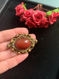 Andriani Vintage is pleased to offer for sale this wonderful example of a Carnelian Colour Cabochon brooch. It has a large central maroon colour cabochon stone  Mounted on a decorative brass like metal alloy base. In an Victorian style  MEASUREMENTS  Size is 5 x 4cms CONDITION In nice vintage condition some minor greening on the brass but nothing that detracts from the original design of this piece  Great unusual item at a very affordable price. Real must have for collectors and fashionistas ali Vintage Gemstone Round Brooches, Vintage Oval Brooch With Cabochon, Vintage Oval Cabochon Brooch, Vintage Pendant Brooches With Cabochon, Vintage Gemstone Cabochons For Gifts, Antique Pendant Brooch With Cabochon, Antique Oval Handmade Brooches, Antique Handmade Oval Brooches, Vintage Brown Jewelry Brooch