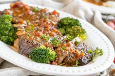 a white plate topped with meat covered in gravy and broccoli on top of a table