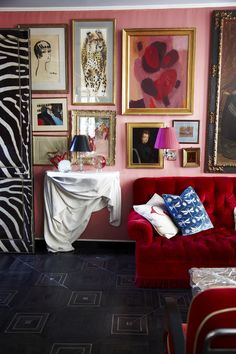 a living room with pink walls and pictures on the wall, red couches in front of a zebra print curtain