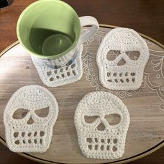 three crocheted sugar skull coasters sitting on top of a table next to a cup