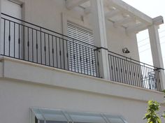 a white building with a black balcony and metal balconies on the second floor