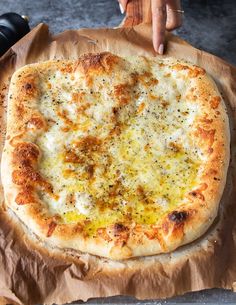 a person holding a pizza on top of a piece of wax paper with yellow sauce