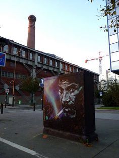 a street corner with a box on the side and a building in the background that has a smokestack painted on it