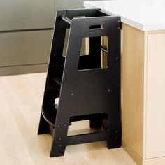 a black step stool sitting on top of a wooden floor next to a white counter