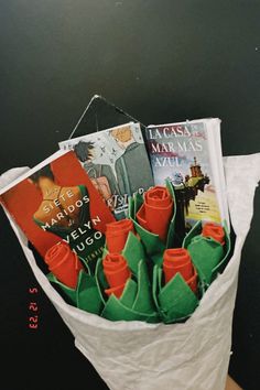 a person holding a paper bag with books in it and some orange roses on the inside