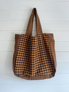 a brown and black checkered tote bag hanging on a white wall with wood planks