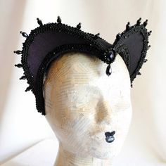 This is a purple and black version of one of most successful designs called Countess. This vampire style headdress is covered with dark purple taffeta and embellished with black cord trimming all around the edges.It is further trimmed with black crystal details that create a halo effect as well as small l beads that were hand-sewn on the trimming to create rich textural interest. The piece is completed with a black crystal handmade element placed at the center front for all that extra drama that Punk Cat Ears For Costume Party, Punk Style Cat Ears For Costume Party, Gothic Costume Accessories For Carnival, Gothic Costume Hats And Headpieces For Masquerade Carnival, Gothic Costume Hats And Headpieces For Carnival, Gothic Costume Hats For Masquerade And Carnival, Gothic Costume Hats And Headpieces For Cosplay, Fitted Black Cat Ears Costume Accessories, Fitted Halloween Costume Accessories With Cat Ears