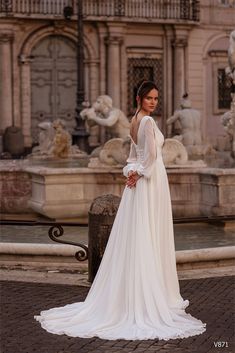 a woman is standing in front of a fountain wearing a wedding dress with long sleeves