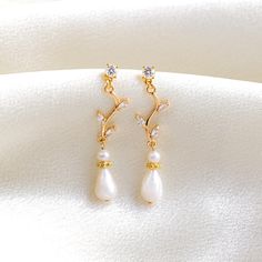 a pair of gold earrings with white pearls and diamonds on top of a white cloth