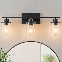 three light bathroom vanity fixture with clear glass shades and black metal frame, on a white wall