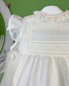 A delicate off-white dress for special occasions, it has a beautiful floral lace detail on the front and two organza sashes on the sides to make bows. The lining is made with a lightweight cotton fabric and the exterior is made with a gorgeous organza fabric and laces. It has buttons on the back for closure. Dry clean 2 piece set Interior: 100% cotton; exterior: 100% polyester Made in Spain Final Sale, no exchanges nor returns are accepted White Gown With Lace Trim And Fitted Bodice, White Lace Dress With Fitted Bodice And Lace Sleeves, White Organza Lace Dress, Sleeveless Lace Gown With Ruffles, White Organza Lace Dress Elegant Style, Elegant White Lace Dress With Organza, Baptism Dress With Lace Bodice And Organza Material, Elegant Sleeveless Organza Lace Dress, White Dress With Lace Sleeves And Fitted Bodice