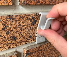 a hand holding an object in front of a brick wall