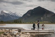 two people standing on a dock in front of mountains