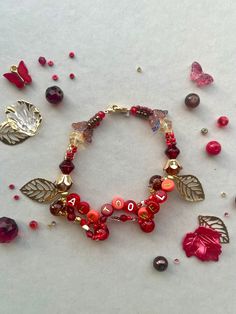 a red bracelet with leaves and letters on it, surrounded by other beads and charms