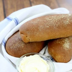 two loaves of bread sitting on top of a white cloth next to a bowl of cream