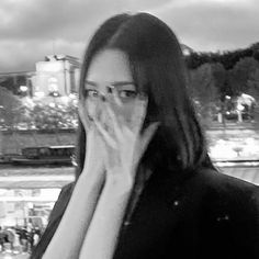 a woman with glasses covering her face in front of a window at night, holding her hand up to her mouth